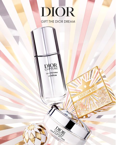 Los productos para el cuidado de la piel de Dior, que incluyen un sérum, una crema y una caja dorada decorativa, se muestran sobre un fondo radiante con rayos de color rosa claro, dorado y blanco. El texto dice: "DIOR. REGALE EL SUEÑO DE DIOR.
