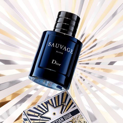 Un frasco azul oscuro del perfume Dior Sauvage Elixir se exhibe frente a un brillante fondo de cielo estrellado, con un mapa decorativo de Christian Dior parcialmente visible en la parte inferior.