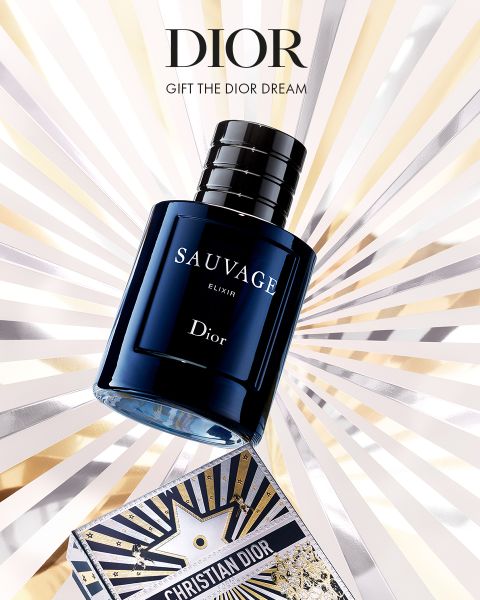 Un frasco del perfume Dior Sauvage Elixir se encuentra sobre una caja decorativa de Dior, de cuyo fondo emergen rayos dorados, plateados y blancos. El texto dice: "Dior. Regale el sueño de Dior".
