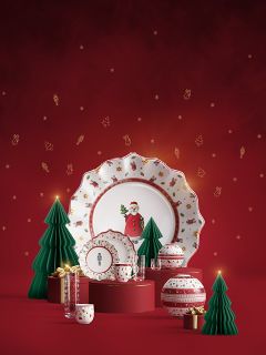 Vajilla festiva con motivos de Papá Noel y navideños exhibida con árboles de papel verdes, cajas de regalo doradas y adornos rojos sobre un fondo rojo con símbolos festivos dorados.