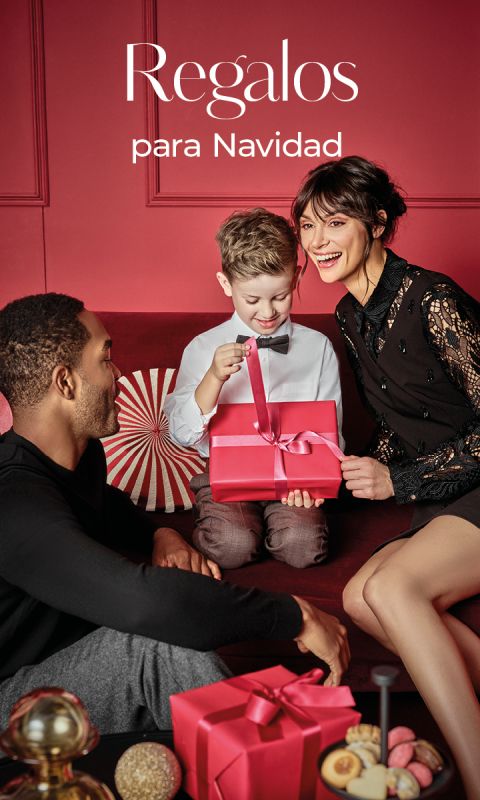 Una familia sonriente está sentada en un sofá rojo intercambiando regalos de Navidad. Un niño pequeño abre un regalo rojo junto a dos adultos. El texto en español de arriba dice "Regalos para Navidad".