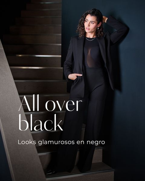 Una mujer con un elegante blazer y pantalones negros está de pie en una escalera y se apoya en la pared. El texto en la imagen dice "All over black" y "Looks glamorosos en negro.".