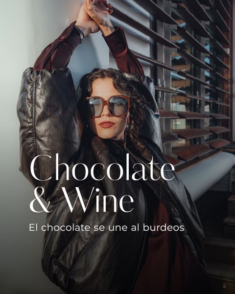 Una mujer con gafas de sol y una chaqueta oscura y grande se apoya en un edificio moderno con listones de metal. El texto en la imagen dice: "Chocolate y vino. El chocolate se une al burdeos."