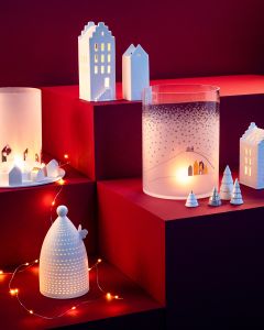 Casas de cerámica, árboles y candelabros están dispuestos en escalones rojos y suavemente iluminados por luces de cadena y luz de velas. La escena recuerda a un ambiente acogedor y festivo de pueblo invernal.