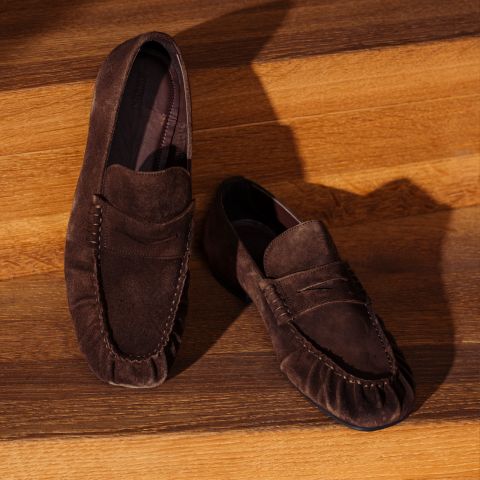 Un par de zapatos marrones de gamuza expuestos en escalones de madera, con la textura resaltada por luces y sombras.