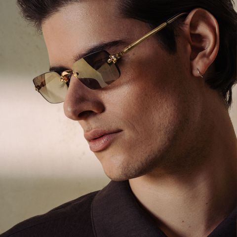 Hombre con gafas de sol de montura dorada y camisa oscura.