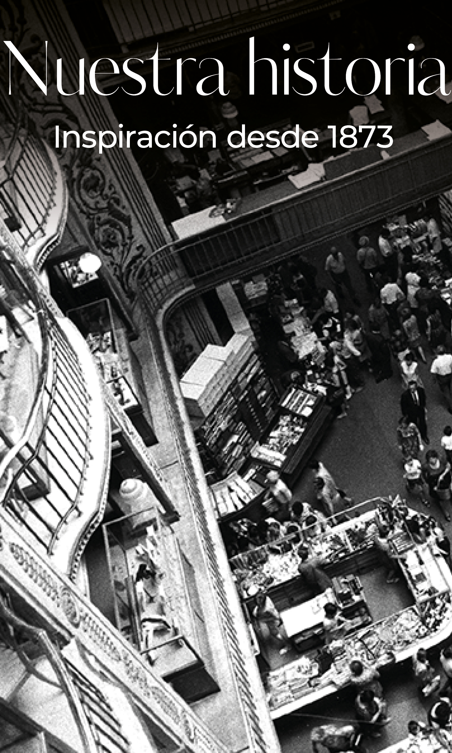 Fotografía en blanco y negro de un mercado cubierto o unos grandes almacenes con balcones y barandillas ornamentadas. El texto en español dice: "Nuestra historia. Inspiración desde 1873.".