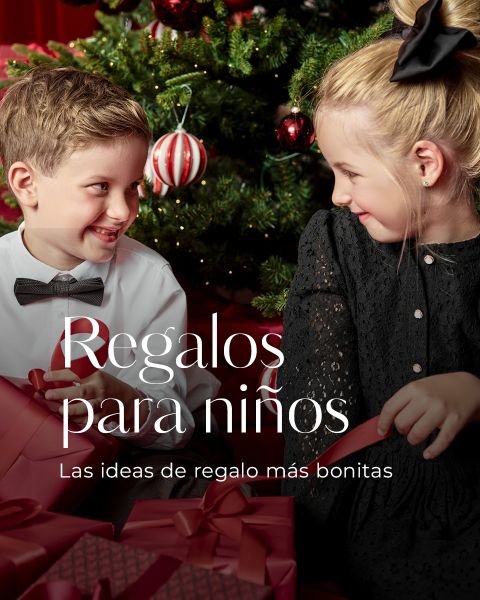 Dos niños, un niño con camisa blanca y pajarita y una niña con un vestido negro, están sentados junto a un árbol de Navidad decorado, se sonríen y sostienen cajas de regalo rojas. El texto en español dice "Regalos para niños".