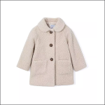 Ein cremefarbener, strukturierter Kindermantel mit rundem Kragen, zwei Vordertaschen und drei braunen Knöpfen auf der Vorderseite auf weißem Hintergrund.