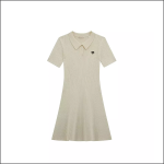 Ein kurzärmeliges, cremefarbenes, geripptes Strickkleid mit Polokragen und einem kleinen schwarzen Herz-Emblem auf der linken Brust, das auf einem schlichten weißen Hintergrund abgebildet ist.