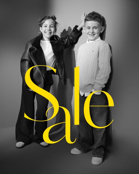 Dos niños sonrientes posan con atuendos elegantes con la palabra "Sale" en grandes letras amarillas sobre la imagen.