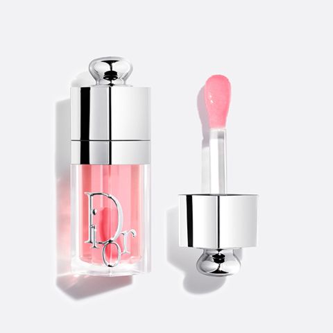 Un tubo de brillo de labios Dior con brillo rosa y tapa plateada, mostrado abierto con el aplicador al lado sobre un fondo blanco.