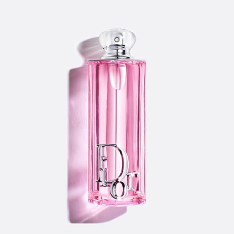 Un frasco de perfume alto y rosa con una tapa transparente y letras plateadas de "Dior" que proyecta una sombra suave sobre un fondo blanco.