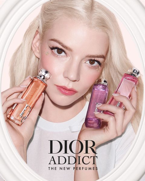 Una mujer con cabello rubio sostiene tres frascos de perfume Dior Addict en tonos naranja, rosa y lila, que incluyen el texto "DIOR ADDICT THE NEW PERFUMES".