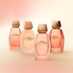 Cuatro frascos del perfume «All of Me» de Narciso Rodriguez en tonos suaves de rosa y beige, dispuestos sobre un fondo claro y suavemente desenfocado.