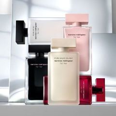 Cinco frascos de perfume de Narciso Rodriguez en negro, blanco, rosa y rojo están de pie y apilados frente a un fondo moderno y reflectante.