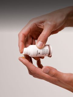 Una persona dispensa una pequeña cantidad de crema o loción de una botella blanca en la punta de su dedo.