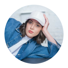 Mujer con gorro blanco y chaqueta vaquera, apoyada en su brazo y mirando a la cámara con expresión neutral.