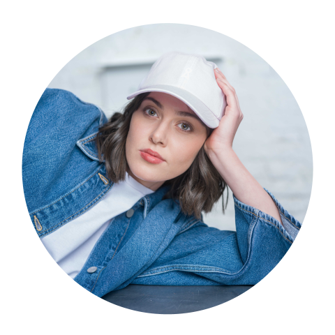 Mujer con gorro blanco y chaqueta vaquera, apoyada en su brazo y mirando a la cámara con expresión neutral.