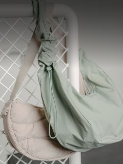 Dos bandoleras, una de color beige claro y otra de color verde pálido, cuelgan de una rejilla metálica blanca sobre un fondo neutro.