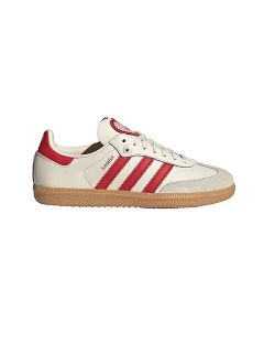 Zapatilla blanca con rayas y talón rojos, suela de goma marrón claro y texto "SAMBA" en el lateral. Diseño clásico de Adidas sobre un fondo blanco liso.
