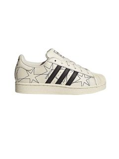 Zapatilla blanca con rayas Adidas negras y contornos abstractos de estrellas negras en los laterales; estilo de caña baja con puntera texturizada.