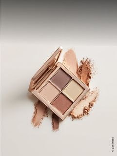 Una paleta de sombras de ojos abierta con cuatro tonos neutros, rodeada de muestras de los polvos sobre una superficie clara.