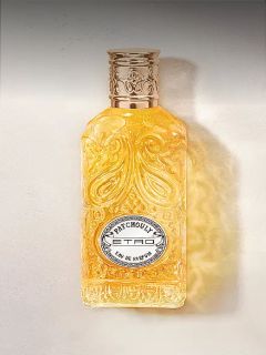 Frasco de vidrio ornamentado con líquido dorado, patrón grabado y etiqueta plateada con la inscripción "Patchouly TRD Eau de Parfum".