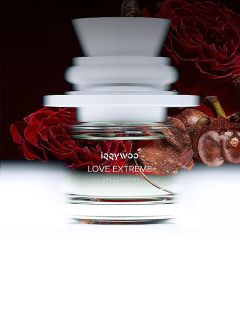 Un frasco de perfume de cristal con la inscripción "LOVE EXTREME" con efecto de movimiento borroso, delante de rosas rojas y un fondo oscuro.