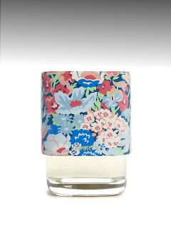 Un frasco de perfume de cristal con un tapón colorido con estampado de flores sobre un fondo gris degradado.