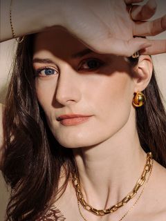 Mujer de piel clara y cabello castaño que lleva joyas de oro y se tapa los ojos con la mano, uno de los cuales es azul y el otro marrón.