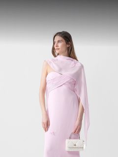 Mujer con un vestido de noche rosa pálido con hombros descubiertos y un bolso blanco frente a un fondo blanco con un degradado gris en la parte superior.