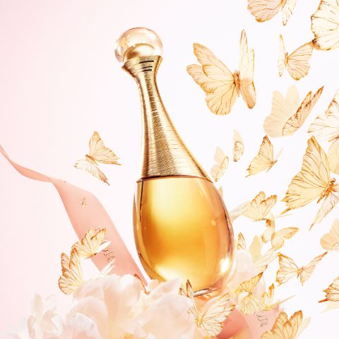 Frasco de perfume dorado, rodeado por una cinta rosa, flores blancas y mariposas doradas revoloteando sobre un fondo de color pastel.