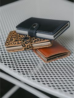 Tres monederos (negro, con estampado de leopardo y marrón) están sobre una mesa de rejilla metálica blanca.