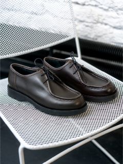 Un par de zapatos de cordones de cuero marrón oscuro está sobre una silla de rejilla metálica blanca.