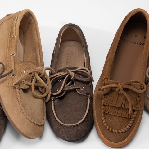 Tres mocasines marrones de ante con cordones están dispuestos uno al lado del otro, cada uno con diferentes costuras y detalles sobre un fondo blanco.