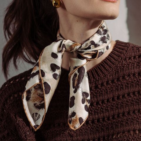 Una mujer lleva un jersey de punto marrón y una bufanda de color crema con estampado de leopardo atada al cuello.