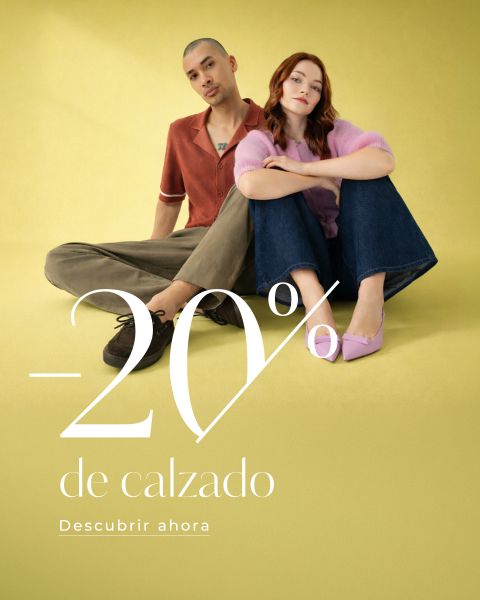 Dos modelos están sentadas en un suelo amarillo, una con una camisa roja y la otra con un jersey rosa. El texto dice "-20% de calzado. Descubrir ahora."