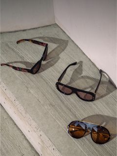 Tres gafas de sol con diferentes monturas y cristales se colocan en escalones de hormigón a la luz del sol frente a una pared blanca.