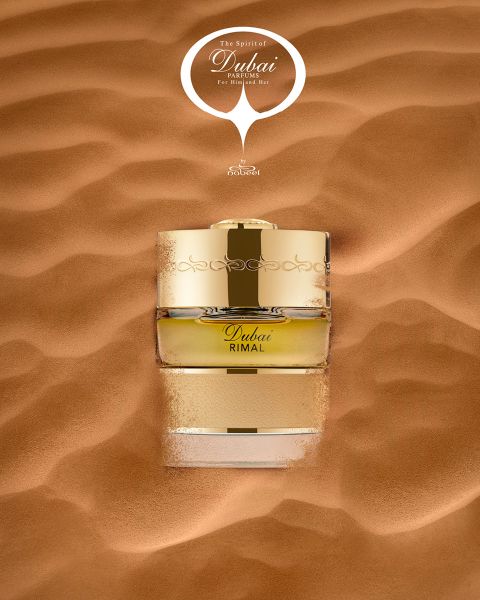 Un frasco de perfume dorado con la inscripción «Dubai Rimal» está parcialmente hundido en la suave arena del desierto, y encima de él se lee la frase «The Spirit of Dubai».