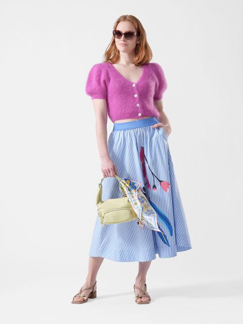 Mujer con top rosa peludo, falda midi azul a rayas con estampado floral, gafas de sol, bolso amarillo con pañuelo y sandalias.