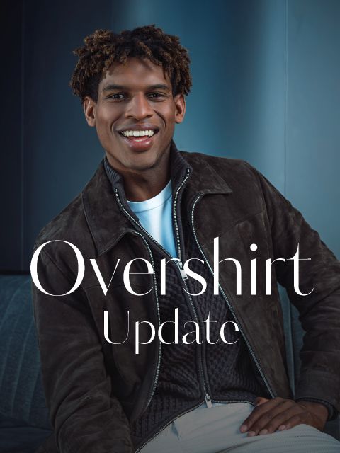 Un hombre sonriente con una sobrecamisa marrón y una camiseta blanca está sentado en un sofá. El texto en la imagen dice: «Actualización de sobrecamisa».