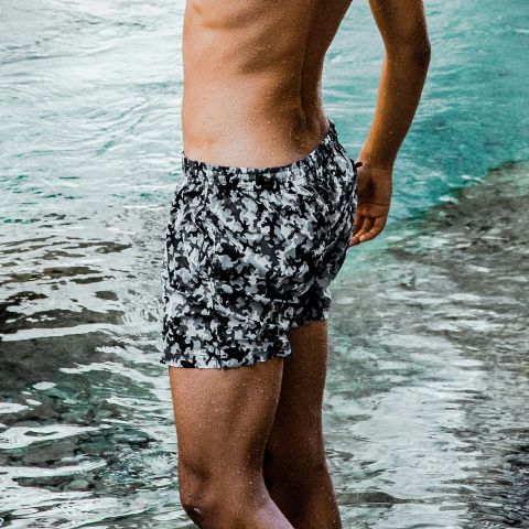 Una persona de pie en aguas poco profundas, vistiendo un bañador de camuflaje blanco y negro, con la parte superior de su cuerpo fuera de la imagen.