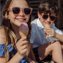Dos niños sonrientes con gafas de sol disfrutan de conos de helado al aire libre en un día soleado.