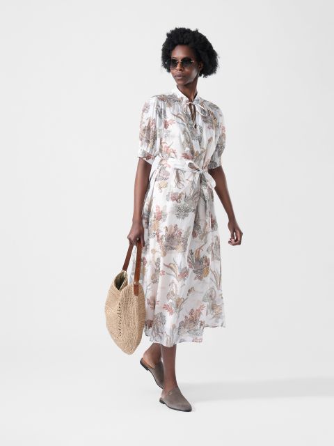Mujer en un vestido midi floreado con lazo en la cintura, con gafas de sol, un bolso tejido en la mano y mocasines marrones.