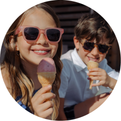 Dos niños sonrientes con gafas de sol disfrutan de conos de helado al aire libre en un día soleado.