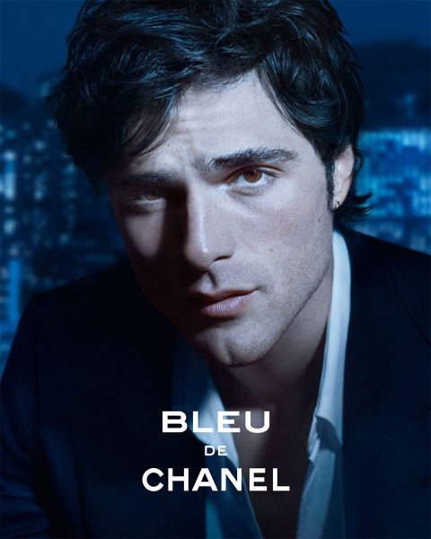 Un hombre con un traje oscuro mira atentamente a la cámara, mientras las luces de la ciudad se difuminan en el fondo; el texto dice "Bleu de Chanel".