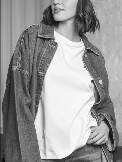Una mujer con chaqueta vaquera y camiseta blanca, posando con una mano en el bolsillo; la imagen está en blanco y negro.