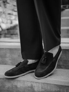 Foto en blanco y negro de una persona que lleva mocasines oscuros con borlas y pantalones de traje, y está de pie en una escalera de hormigón al aire libre.