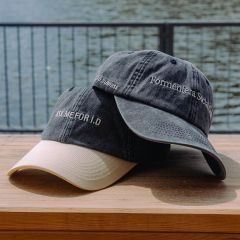 Dos gorras de béisbol en una superficie de madera junto al agua; en una de ellas se lee "ASK ME FOR ID" y en la otra "Formentera Social Club".